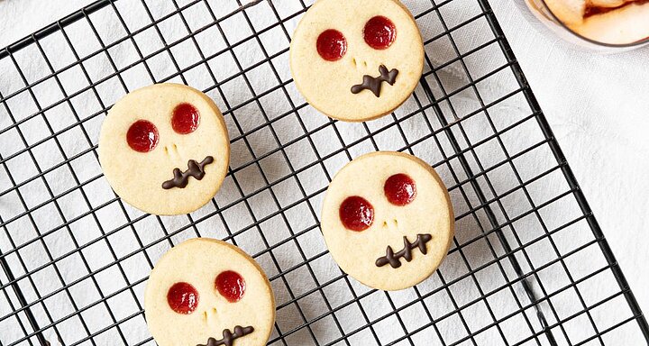 Čtyři kulaté sušenky s červenýma očima a čokoládovými ústy se položí na chladicí mřížku.