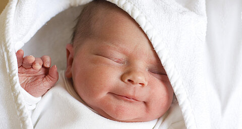 Novorodenec je zabalený do bielej látky a má zdvihnutú ruku.