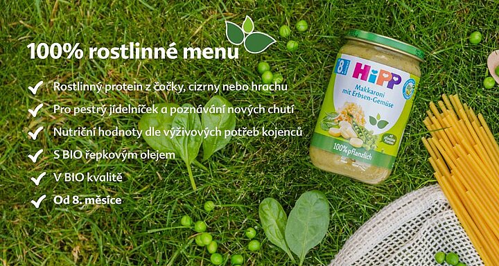 Na travnaté ploše je položena sklenice s dětskou výživou, obklopená čerstvou zeleninou a síťovým sáčkem, vlevo od ní je seznam funkcí v cizím jazyce.