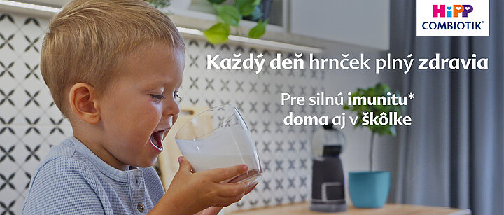 Malé dieťa pije z pohára v modernom kuchynskom prostredí.