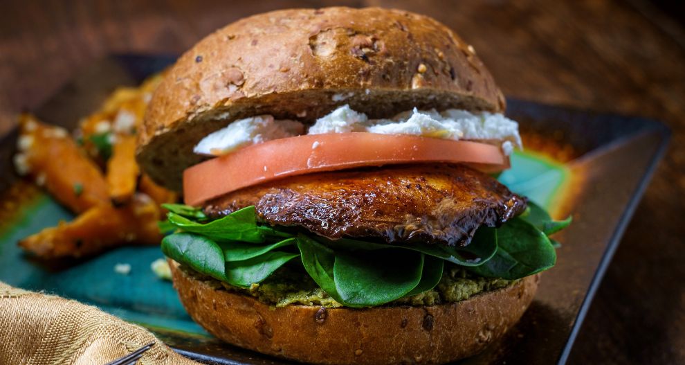 Na talíři se podává burger s grilovanou placičkou, čerstvým špenátem, rajčaty a smetanovou pomazánkou, ke kterému se podávají hranolky ze sladkých brambor.