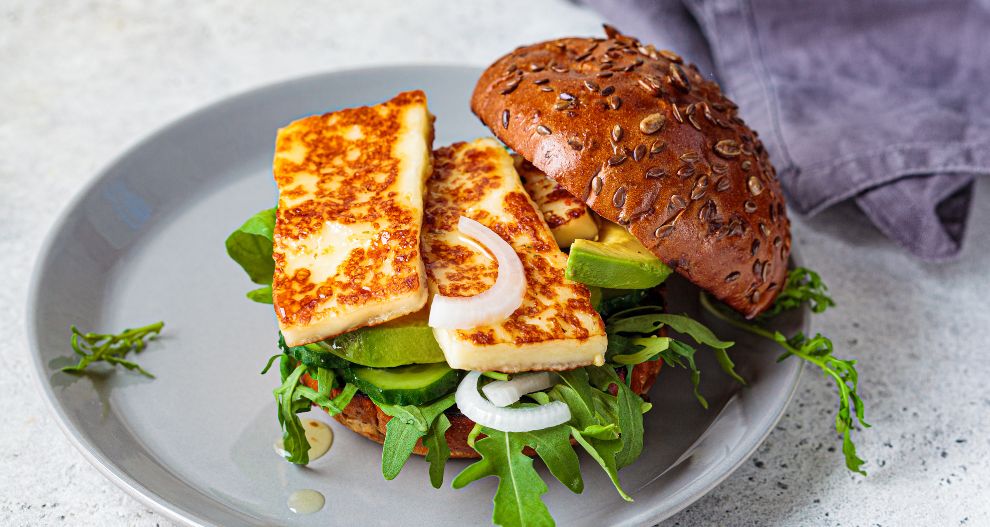 Sendvič s houskou se semínky, obložený čerstvou zeleninou, avokádem a plátky grilovaného sýra.