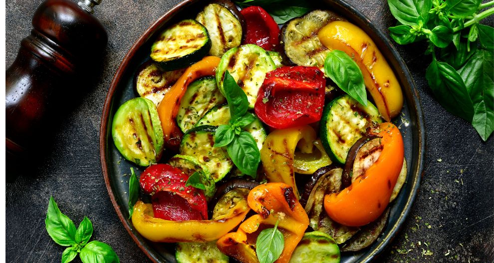 Talíř grilované zeleniny s lístky bazalky a mlýnkem na pepř.