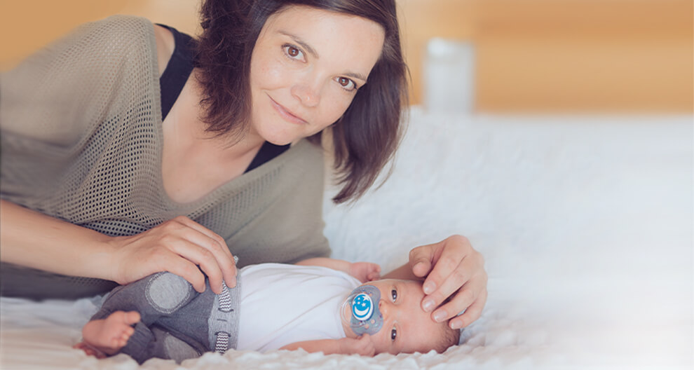 Žena leží na posteli a dívá se na dítě, které leží vedle ní.