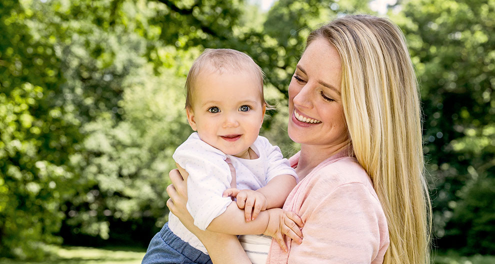 A woman holds a baby in an outdoor setting.