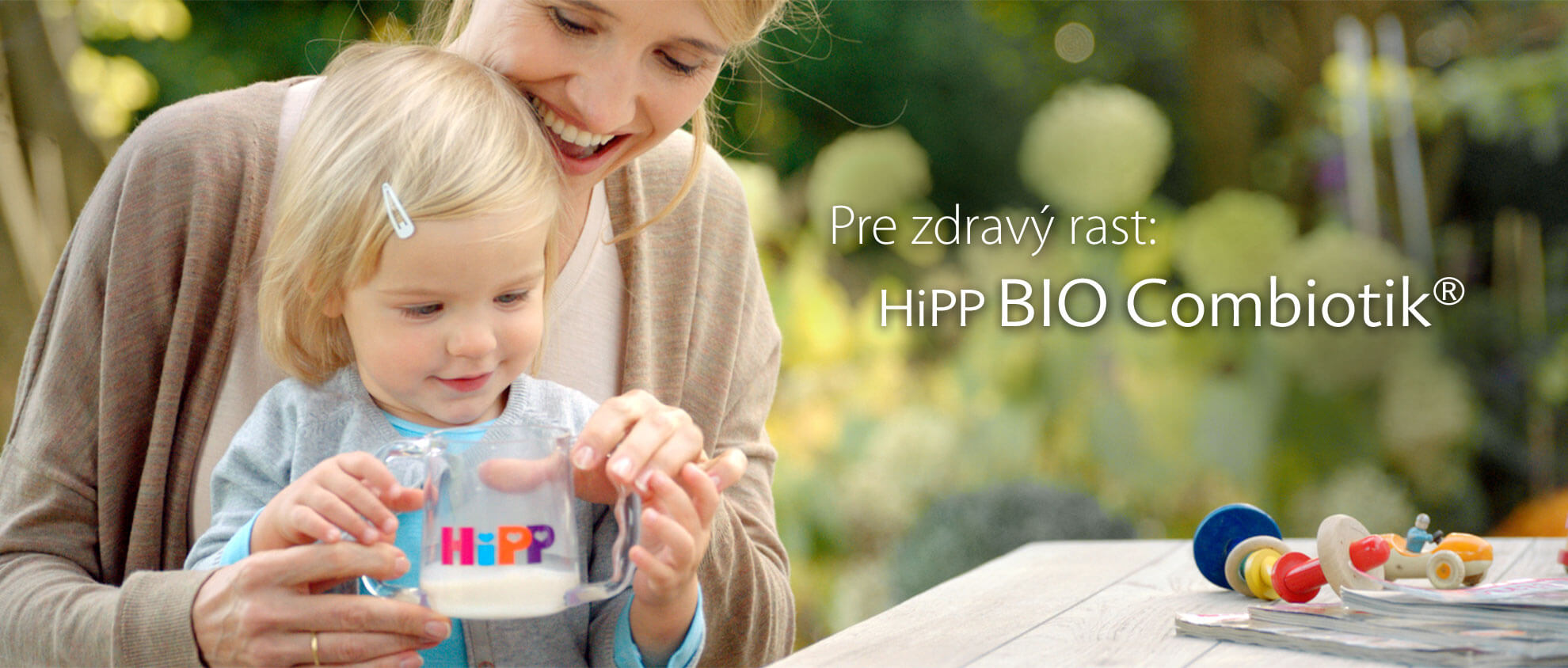 Žena a malé dieťa sú vonku, žena drží sklenenú nádobu s textom "HiPP" a dieťa sa na ňu pozerá.