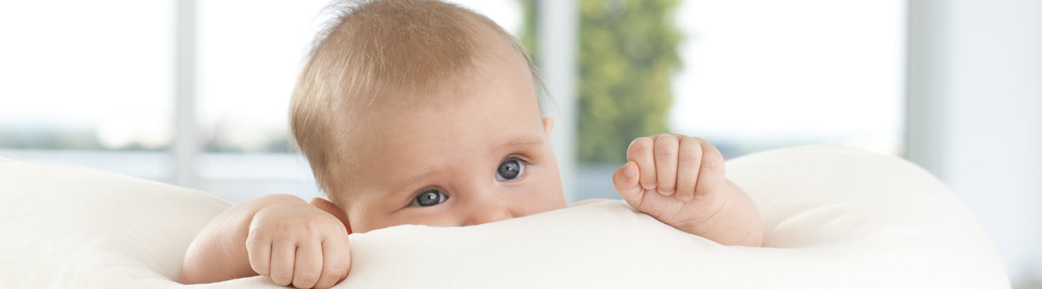 Dieťa s modrými očami vykúka cez bielu prikrývku.