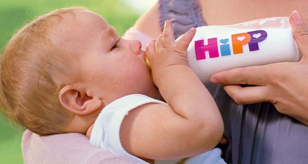 Dieťa pije z fľaše s nápisom "HiPP".