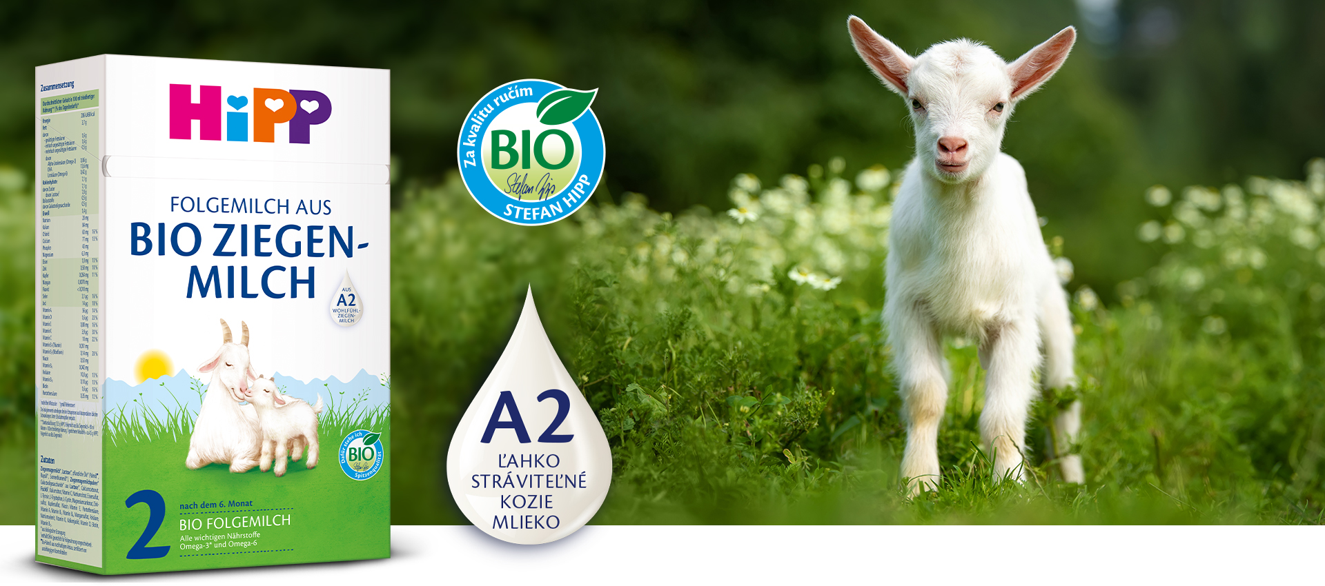 Biela koza stojí na zelenej lúke s bielymi kvetmi vedľa škatule s detskou výživou Hipp s nápismi "Bio Ziegenmilch" a "A2", na ktorej je kvapôčková grafika s nápisom "L'AHKO STRAVITELNE KOZIE MLEKO".