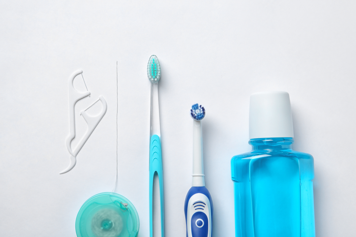 Zbierka predmetov dentálnej hygieny vrátane manuálnej zubnej kefky, elektrickej zubnej kefky, zubnej nite a fľaše ústnej vody.