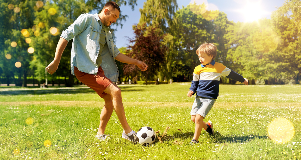 Muž a malý chlapec hrajú v parku futbal.