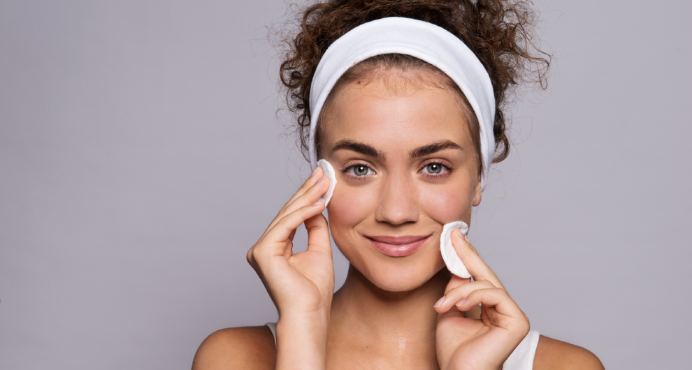 Žena s kučeravými vlasmi a bielou čelenkou si odstraňuje make-up bielym vatovým tampónom.