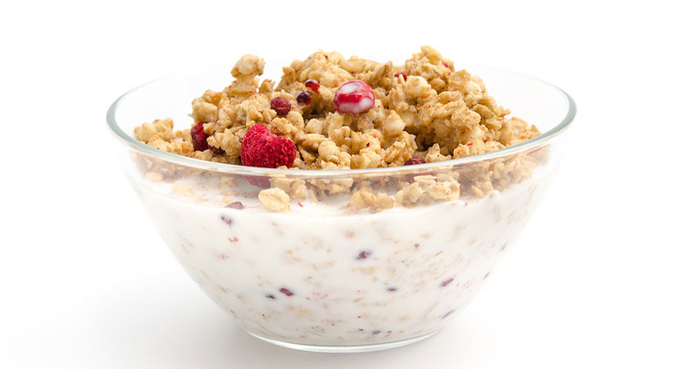 Priehľadná miska naplnená müsli a červenými bobuľami, čiastočne ponorená do bielej tekutiny.
